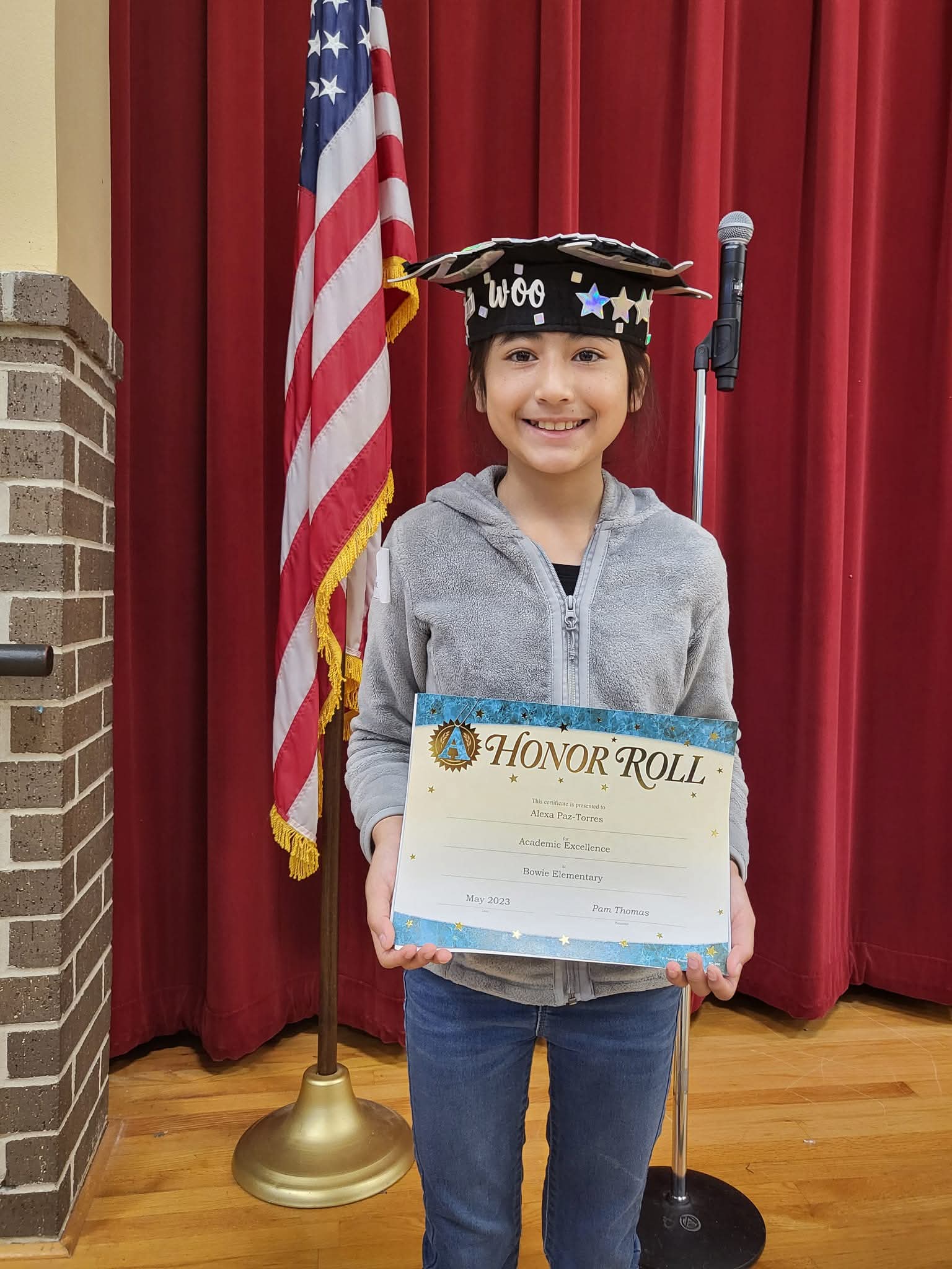Alexa proudly holding an Honor Roll certificate on a school stage